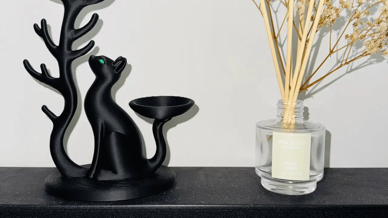 Matte black branch jewelry stand with two cat figures and a ring dish, on a candlelit shelf