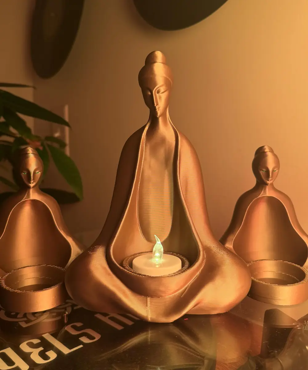 Three brass-finish meditating figures each cradling a lit tea light on a warm shelf
