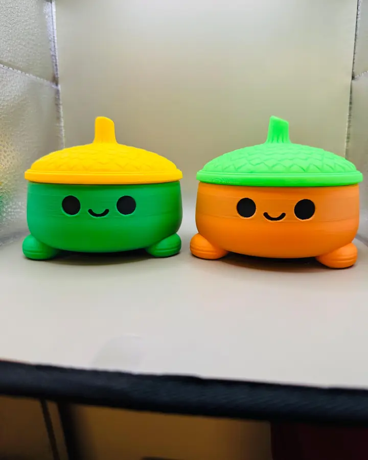Two small lidded 3D printed storage pots with moulded faces, in orange and green